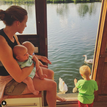 Helen sits to the left of the image, with her two twins perched on her knee. Her young son brogan is at her feet, looking out of a door way to feed the ducks on the river below. The sun streams onto them and the river shimmers